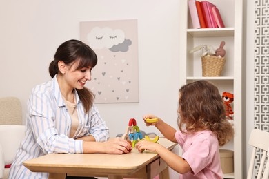 Photo of Autism therapy. Smiling psychologist and little girl playing with educational toy at table in mental health center