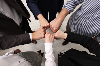 Photo of Teamwork. Group of people joining fists together indoors, top view