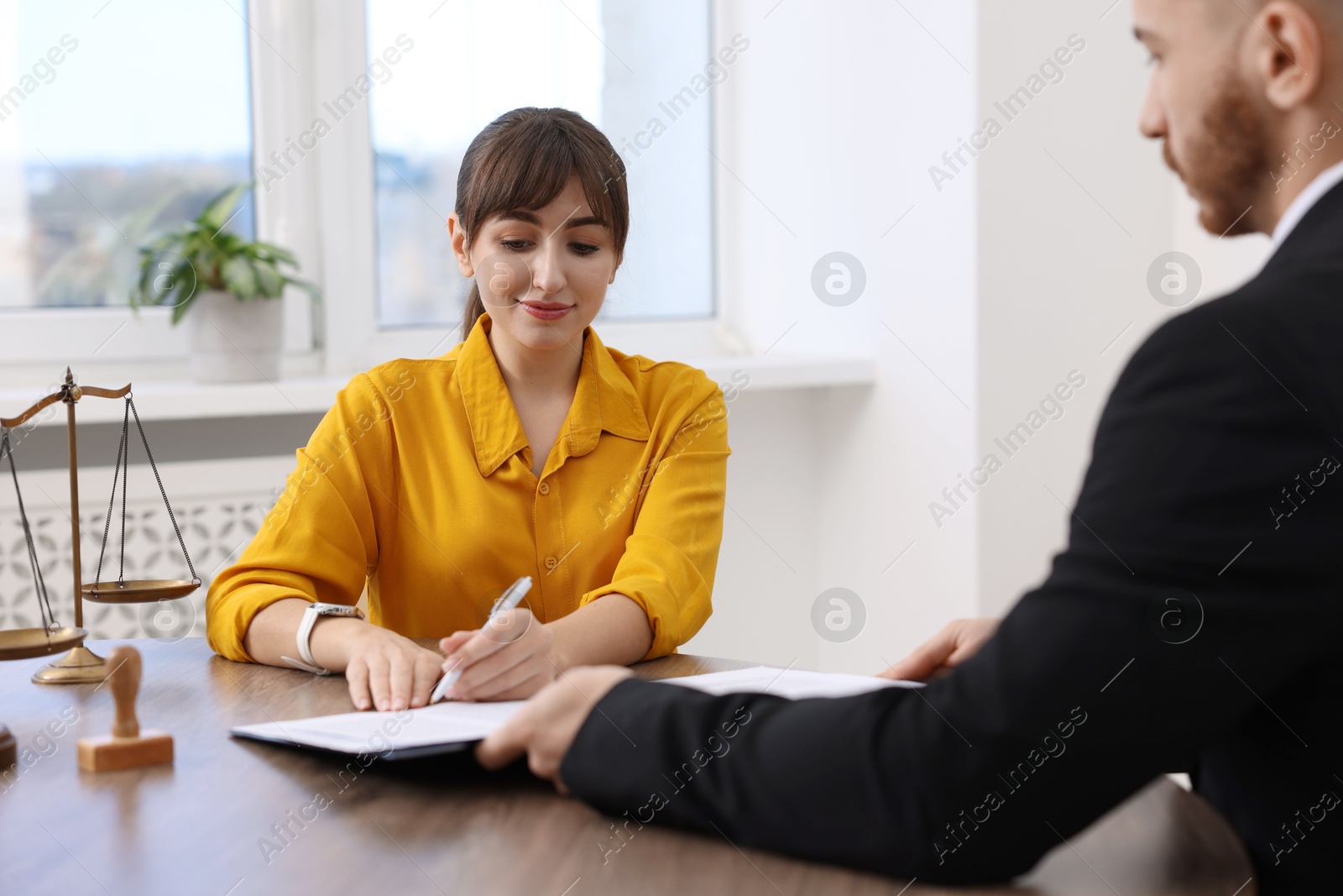 Photo of Client signing notarial paperwork during meeting with lawyer at wooden desk indoors