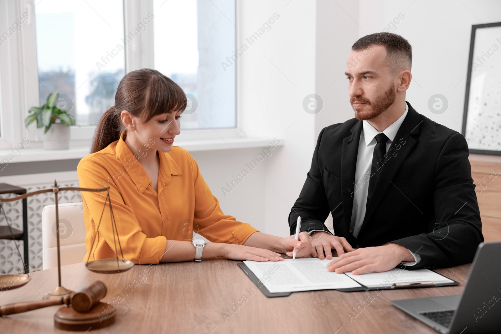 Photo of Client signing notarial paperwork during meeting with lawyer at wooden desk indoors