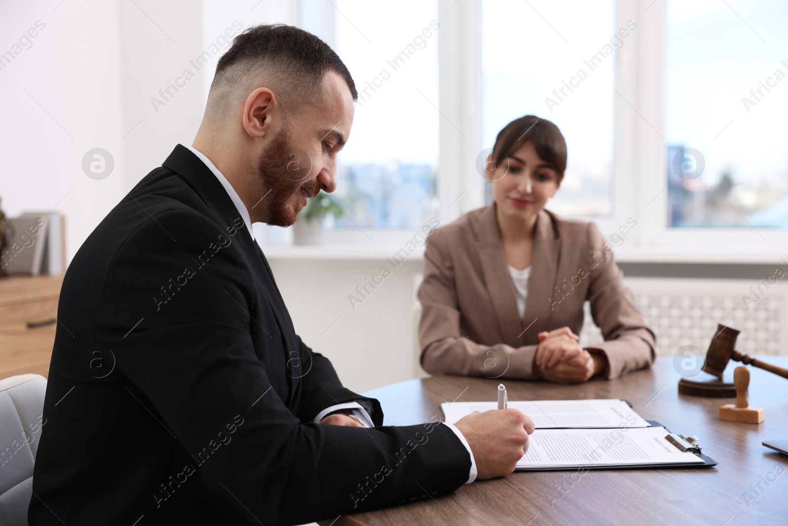 Photo of Client signing notarial paperwork during meeting with lawyer at wooden desk indoors, selective focus