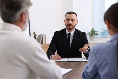 Photo of Man and woman having meeting with professional notary at wooden desk indoors