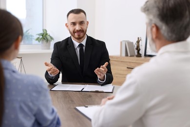 Man and woman having meeting with professional notary at wooden desk indoors