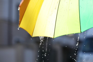 Photo of Open bright umbrella under pouring rain outdoors, closeup