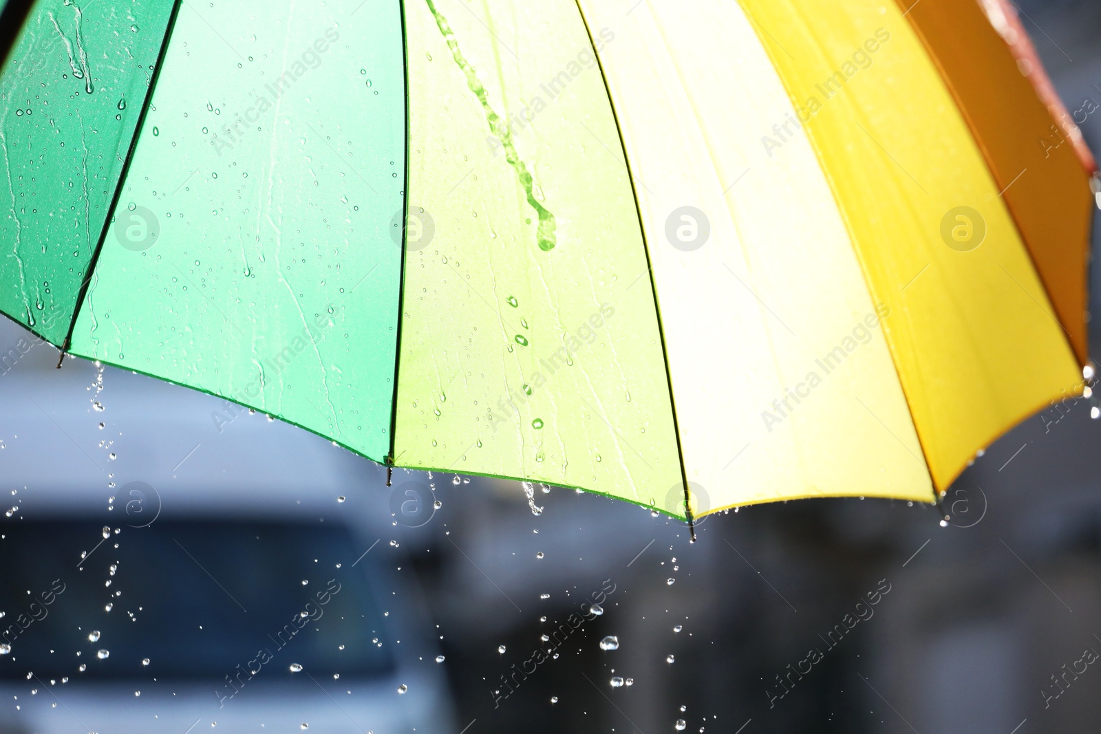 Photo of Open bright umbrella under pouring rain outdoors, closeup