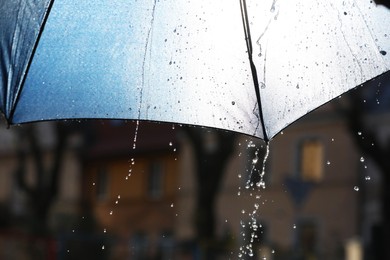 Photo of Open umbrella under pouring rain outdoors, closeup