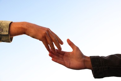 Photo of Man offering helping hand to his friend against blue sky, closeup