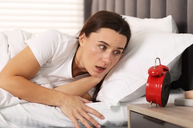 Photo of Overslept woman with alarm clock in bed at home