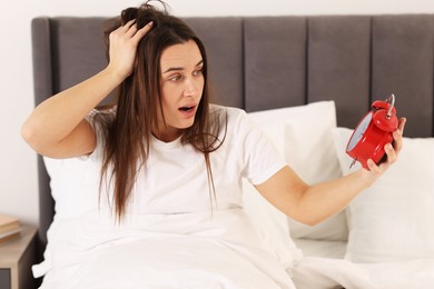 Overslept woman with alarm clock in bed at home