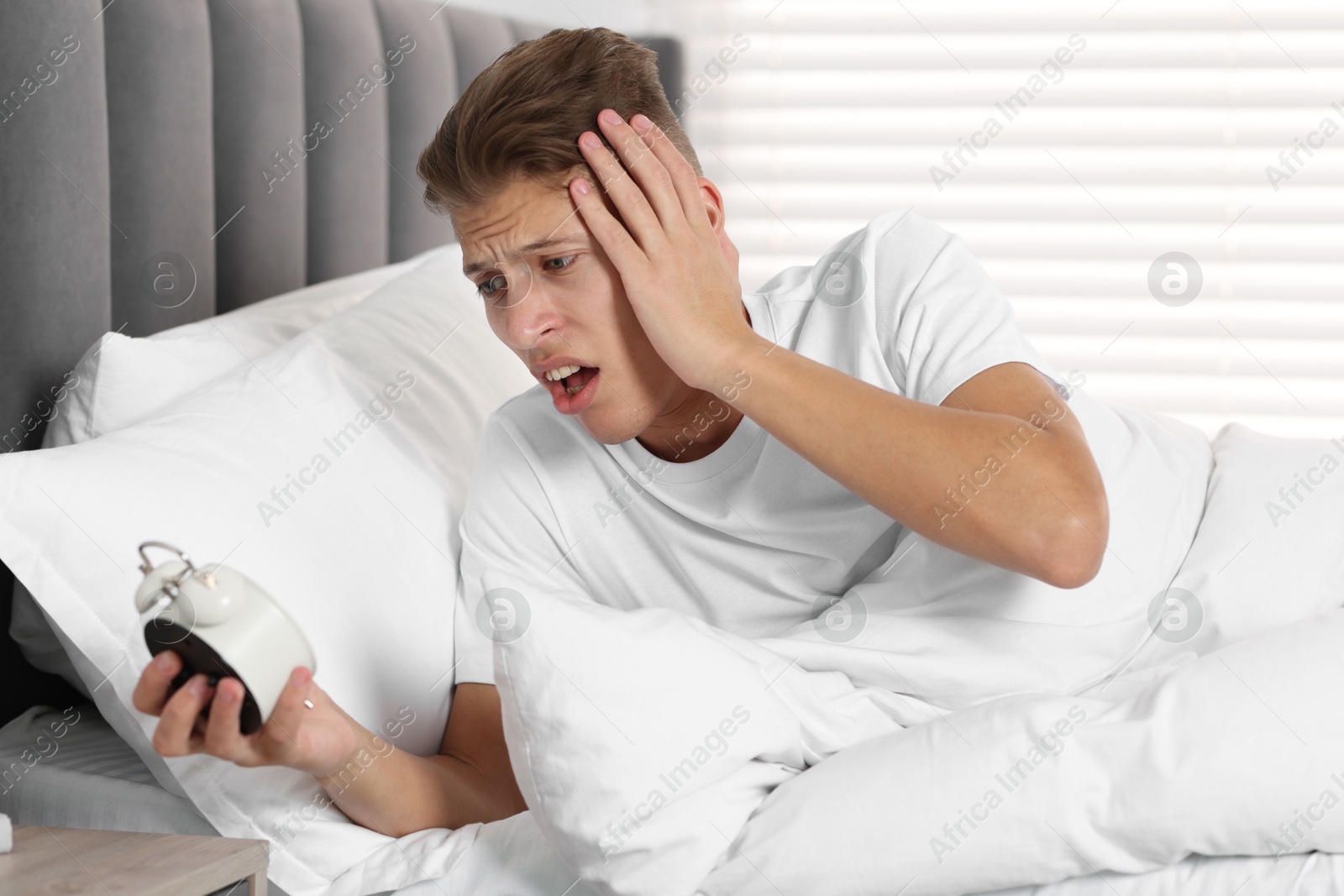 Photo of Overslept man with alarm clock in bed at home