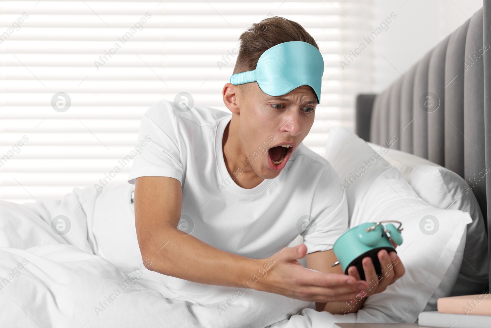 Photo of Overslept man with alarm clock in bed at home