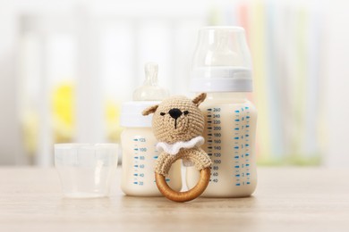 Photo of Feeding bottles with milk and rattle on wooden table indoors