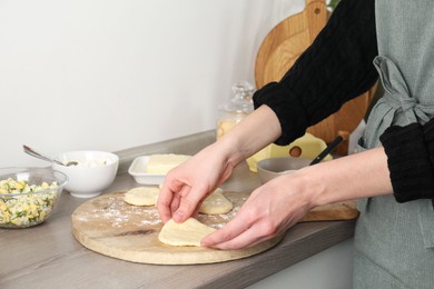 Photo of Woman making pirozhki (stuffed pastry pies) at countertop indoors, closeup