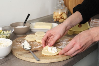 Photo of Woman making pirozhki (stuffed pastry pies) with cottage cheese at countertop indoors, closeup