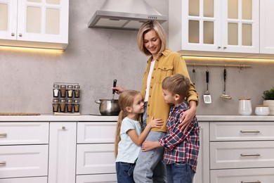 Photo of Happy housewife cooking on stove while her kids playing in kitchen