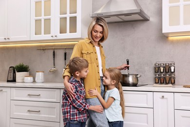 Photo of Happy housewife cooking on stove while her kids playing in kitchen