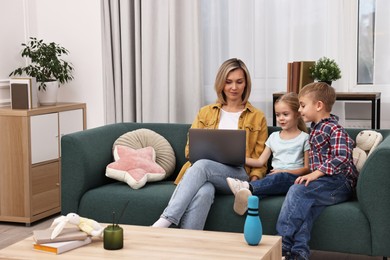 Photo of Housewife spending time with her kids and using laptop on couch at home