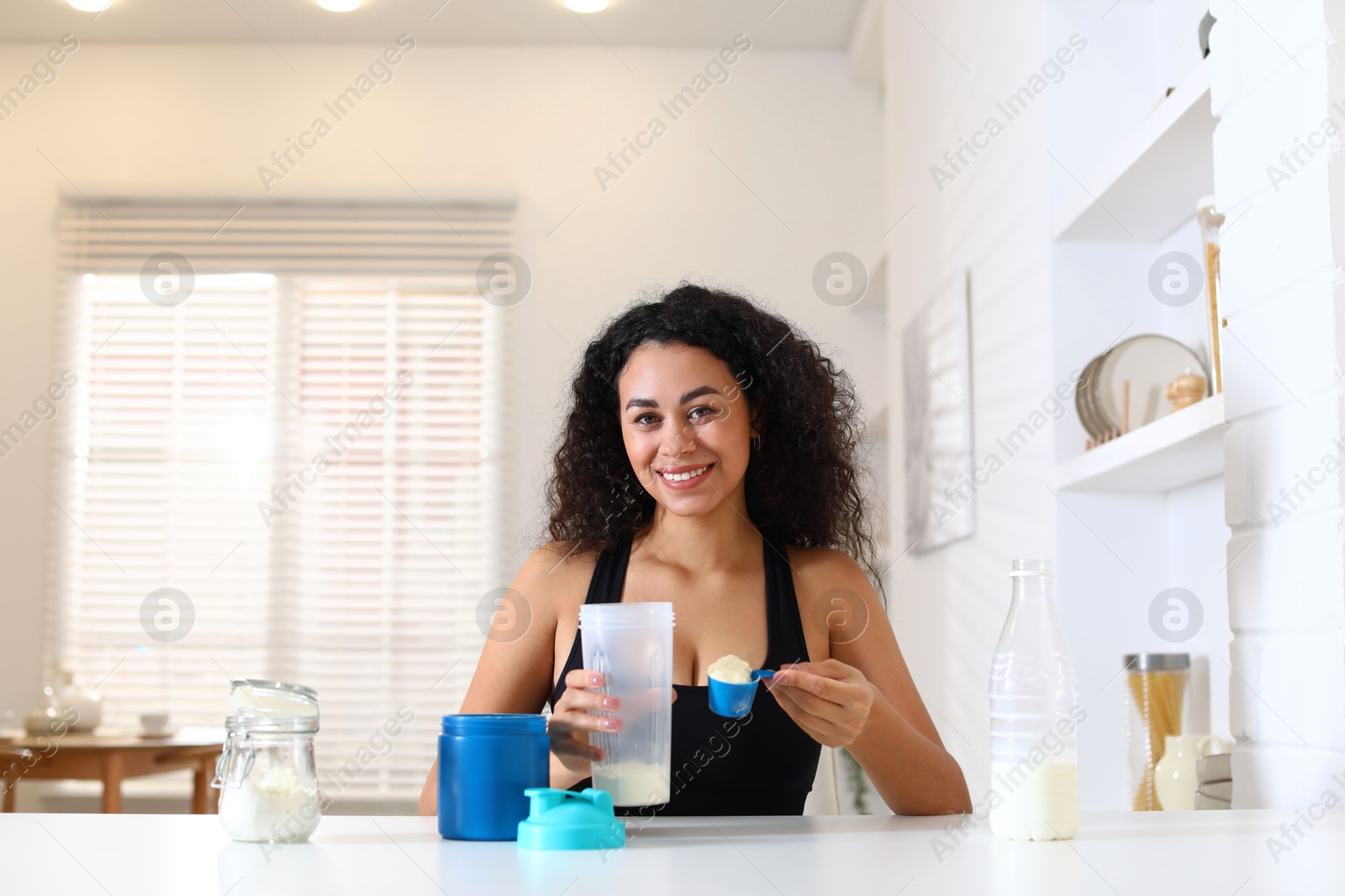 Photo of Beautiful woman making protein shake at white table indoors