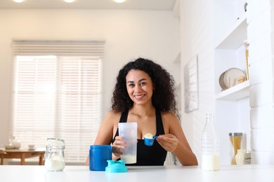 Photo of Beautiful woman making protein shake at white table indoors