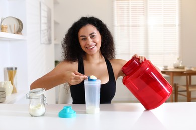 Photo of Beautiful woman making protein shake at white table indoors