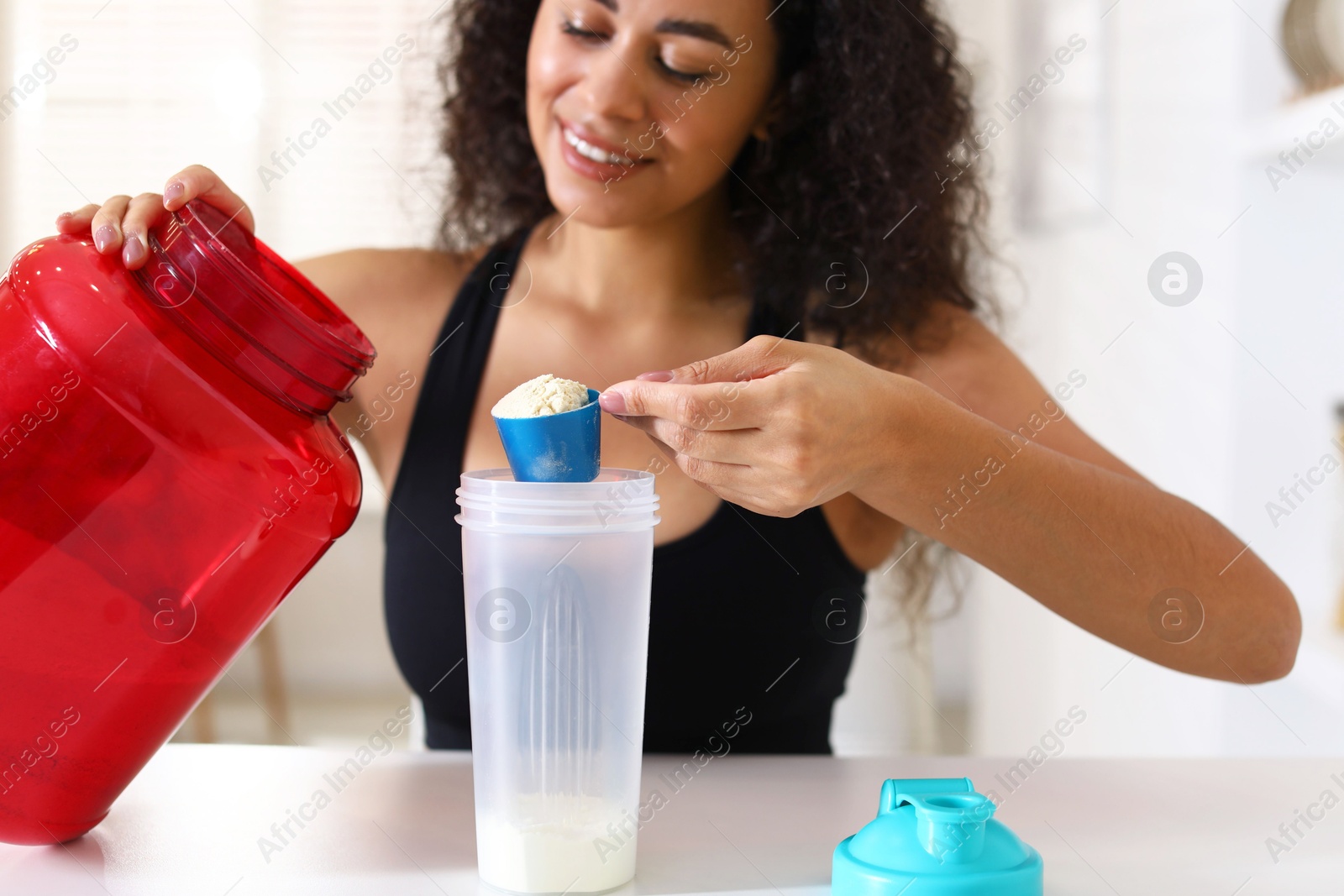 Photo of Beautiful woman making protein shake at white table indoors, closeup