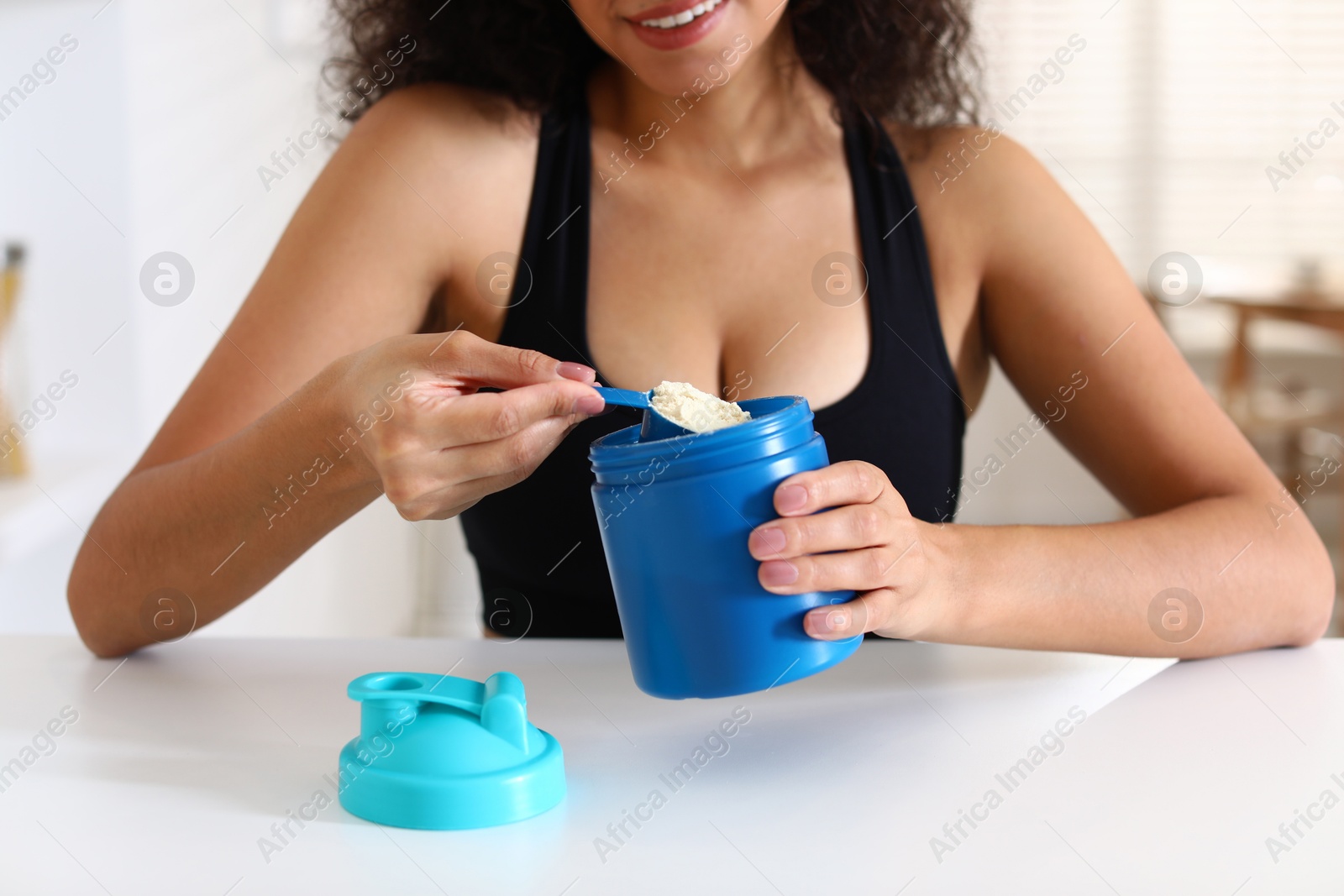 Photo of Beautiful woman making protein shake at white table indoors, closeup