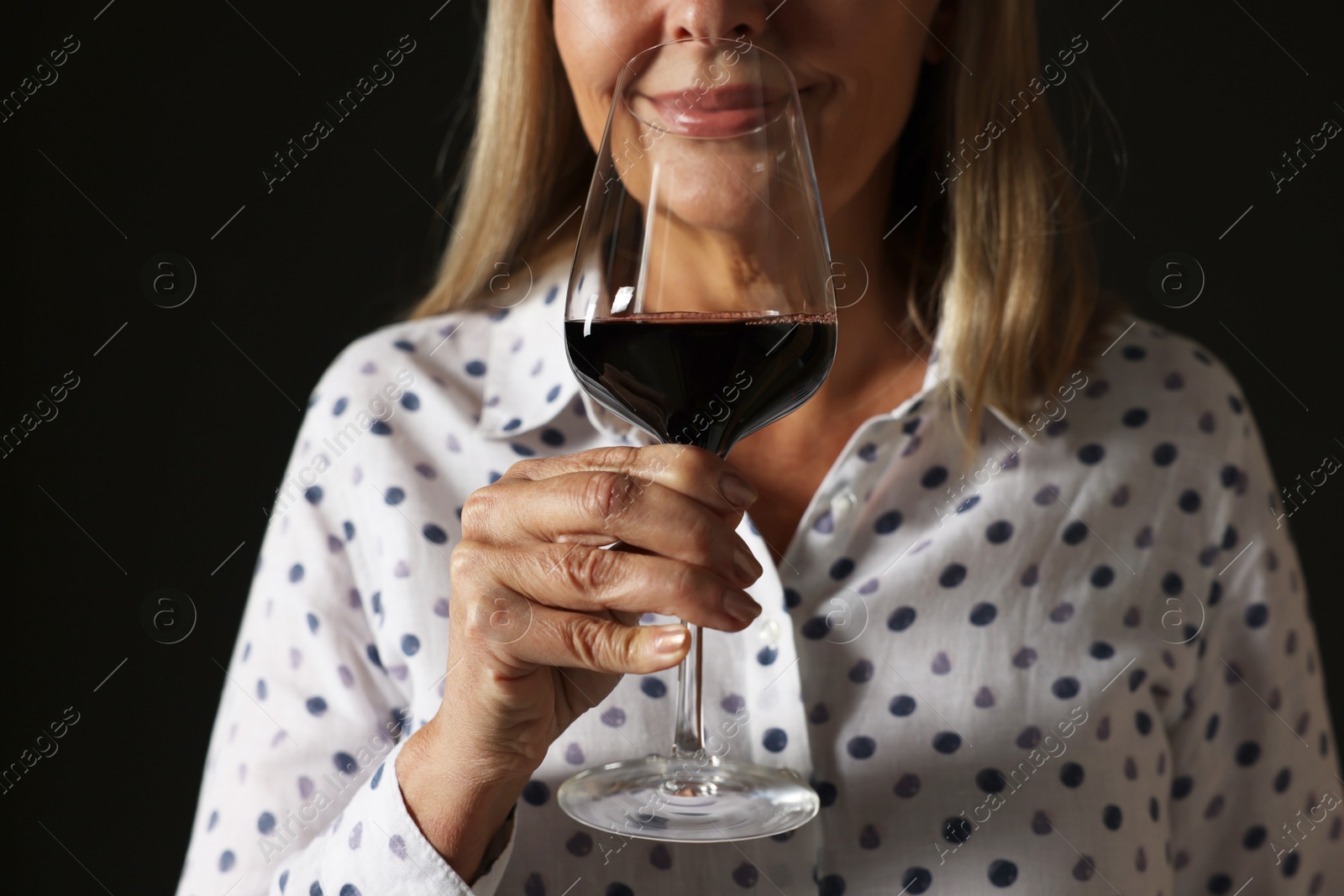 Photo of Professional sommelier tasting red wine in glass on black background, closeup