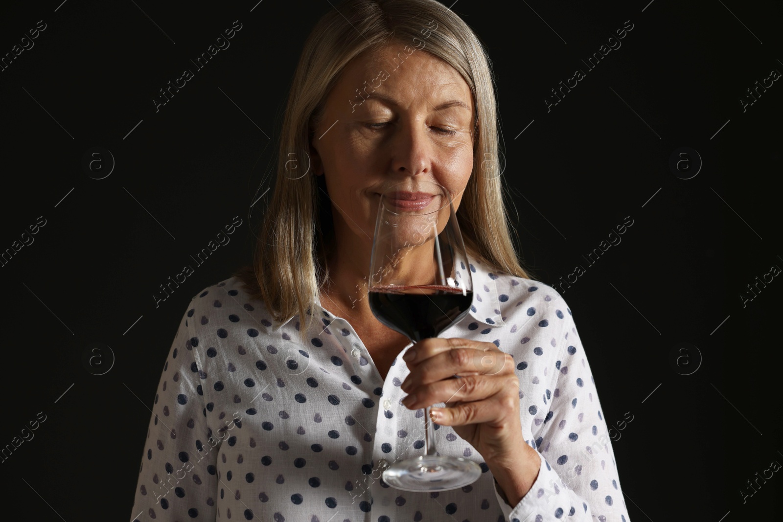 Photo of Professional sommelier tasting red wine in glass on black background