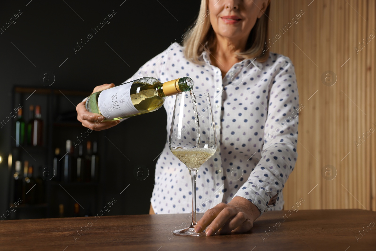 Photo of Professional sommelier pouring white wine into glass at wooden table indoors, closeup