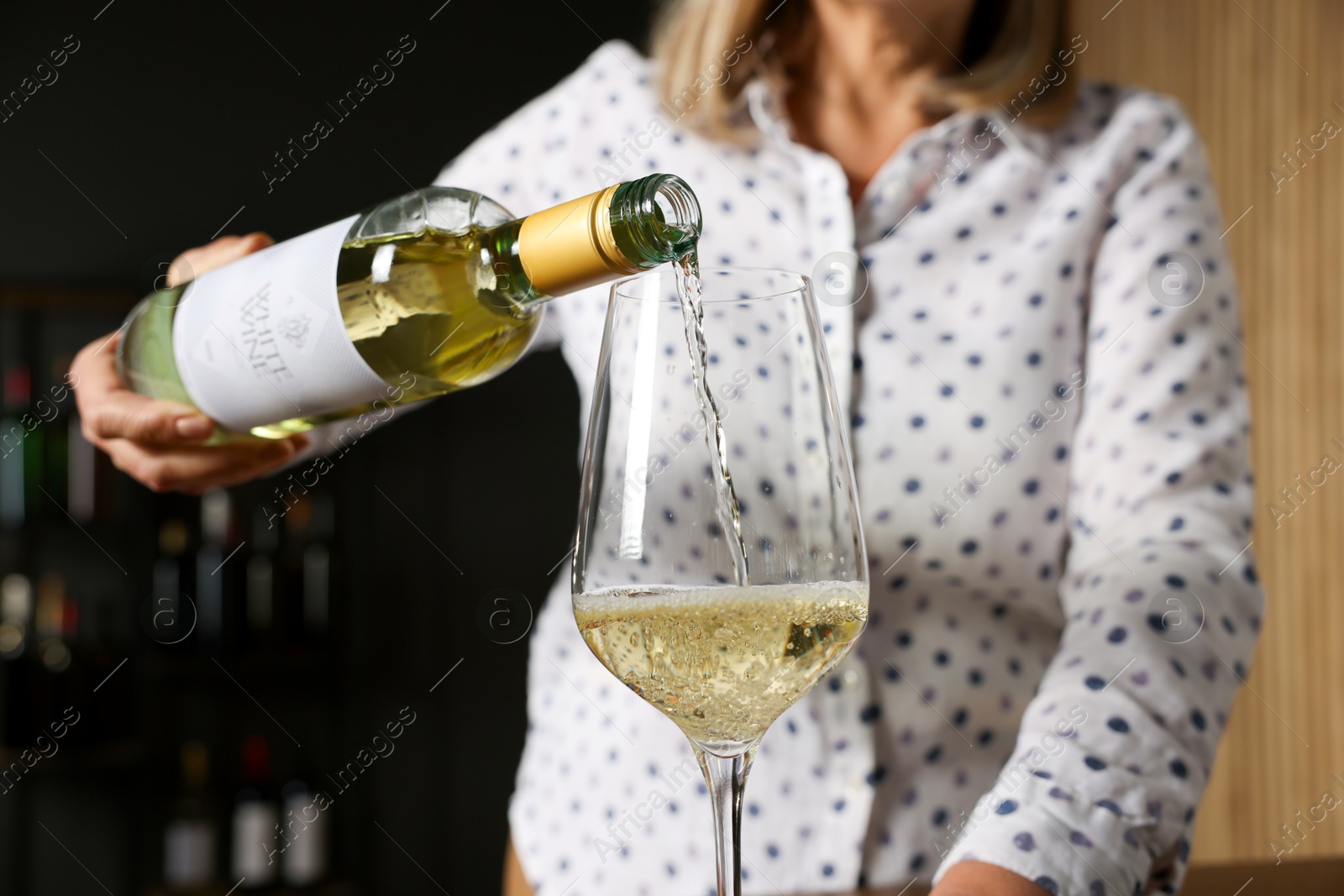 Photo of Professional sommelier pouring white wine into glass indoors, closeup