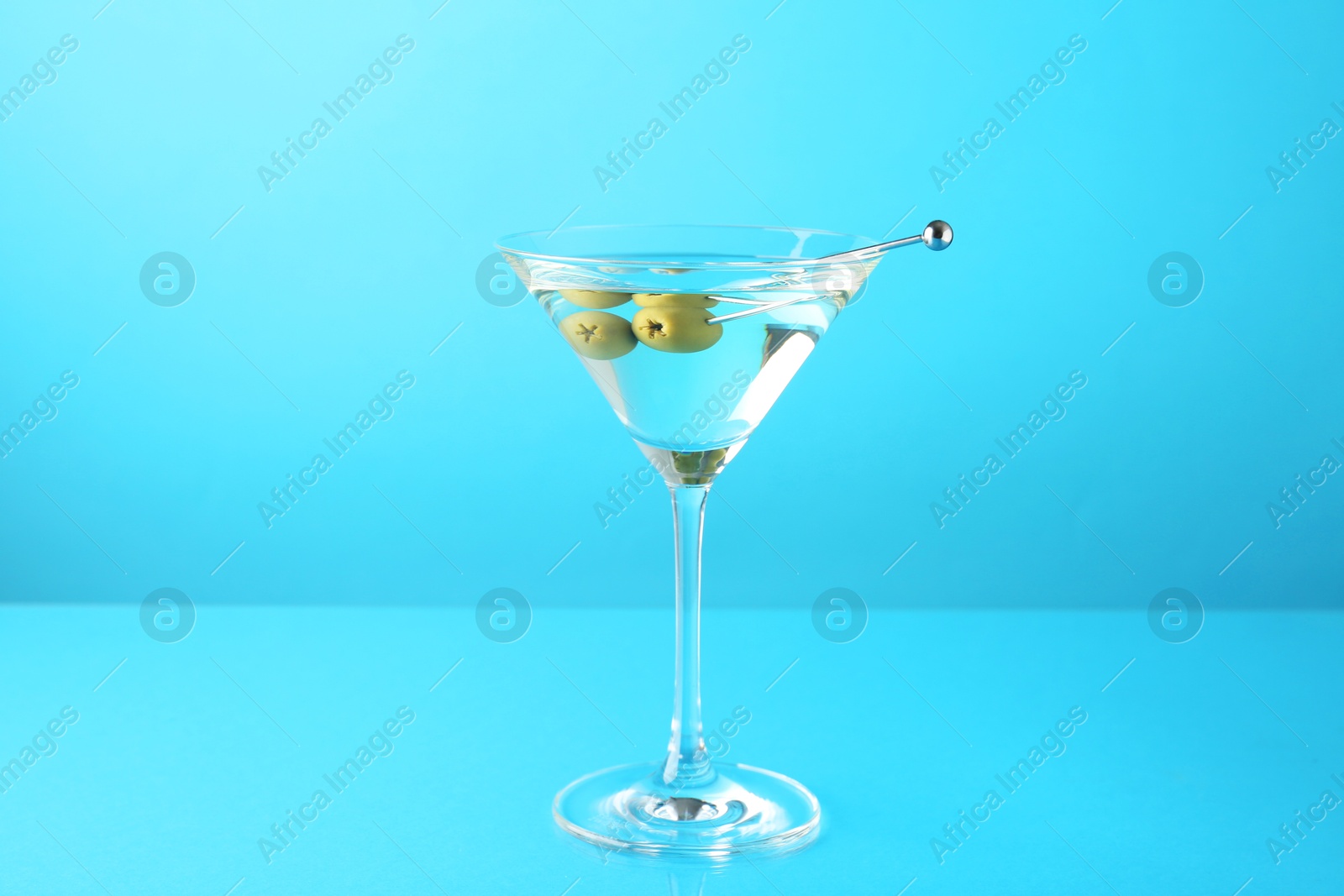 Photo of Martini cocktail with olives in glass on light blue background