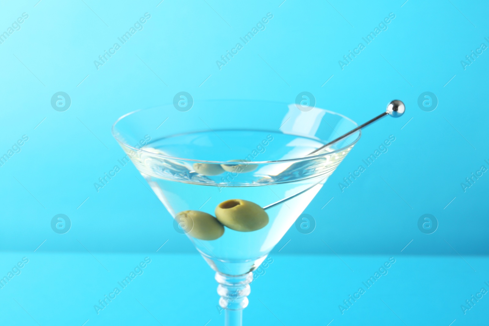 Photo of Martini cocktail with olives in glass on light blue background, closeup