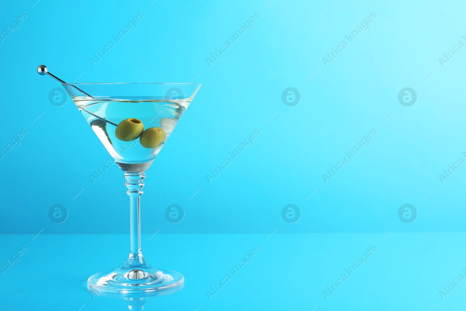 Photo of Martini cocktail with olives in glass on light blue background, space for text