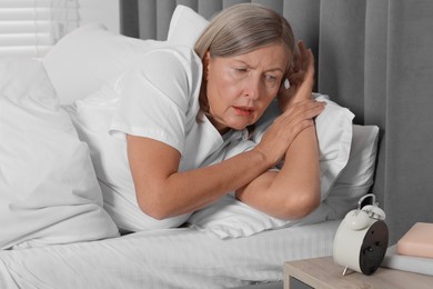 Photo of Overslept woman looking at alarm clock in bed indoors