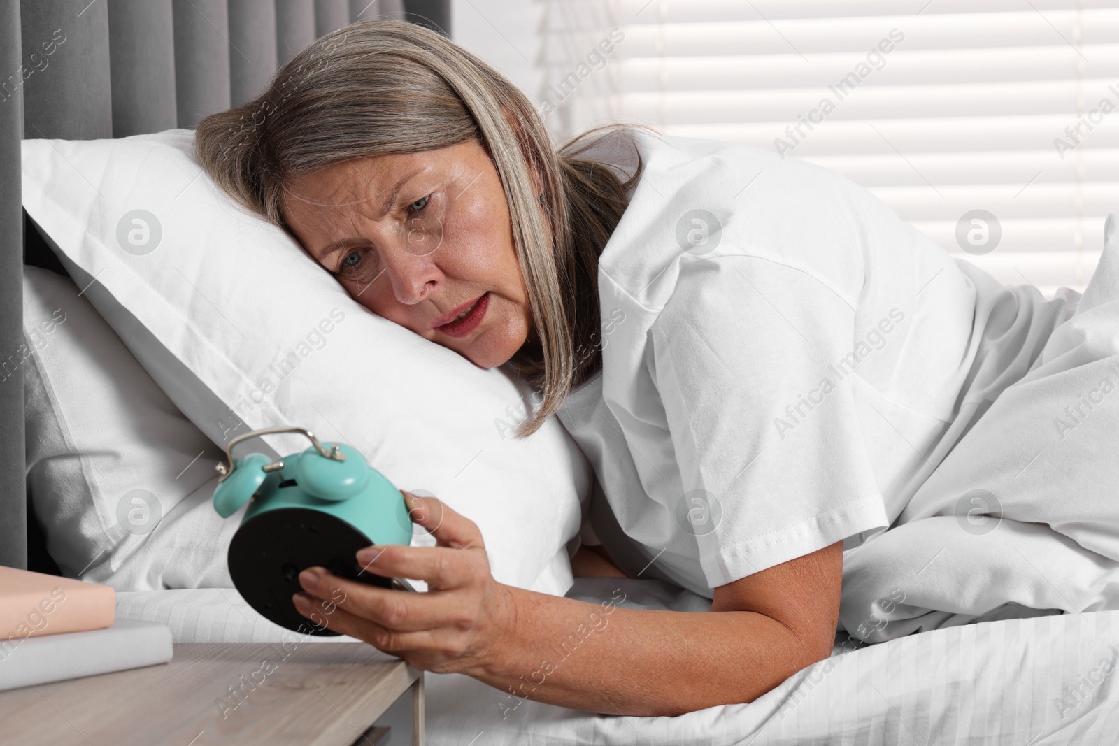 Photo of Overslept woman looking at alarm clock in bed indoors