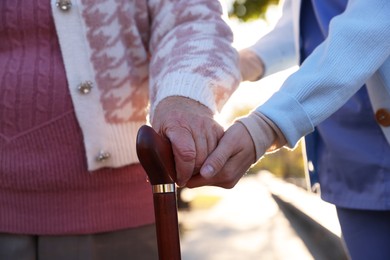 Photo of Elderly woman with walking cane and her caregiver in park, closeup