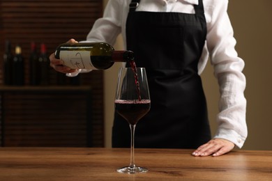 Photo of Professional sommelier pouring red wine into glass at wooden table indoors, closeup