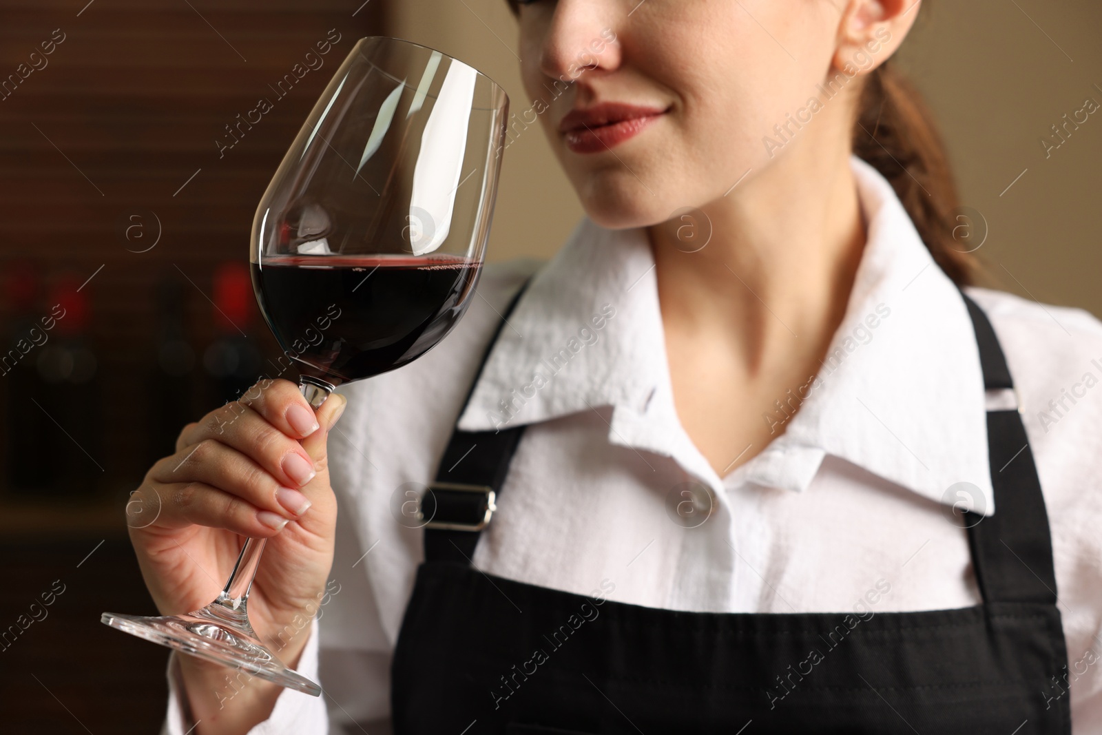 Photo of Professional sommelier tasting red wine in glass indoors, closeup