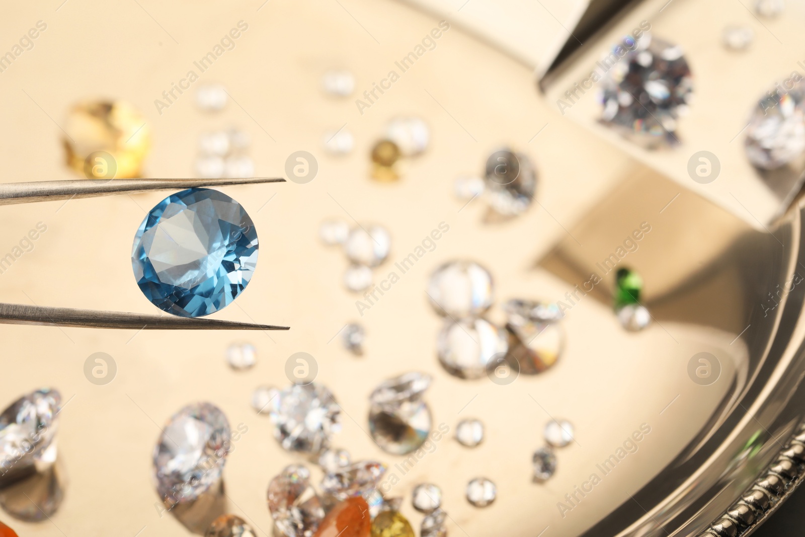 Photo of Tweezers with beautiful gemstone on blurred background, closeup