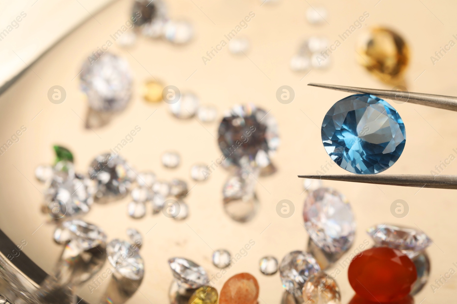 Photo of Tweezers with beautiful gemstone on blurred background, closeup