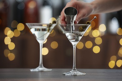 Photo of Woman making tasty martini cocktail with olives at wooden table on blurred background, closeup. Bokeh effect