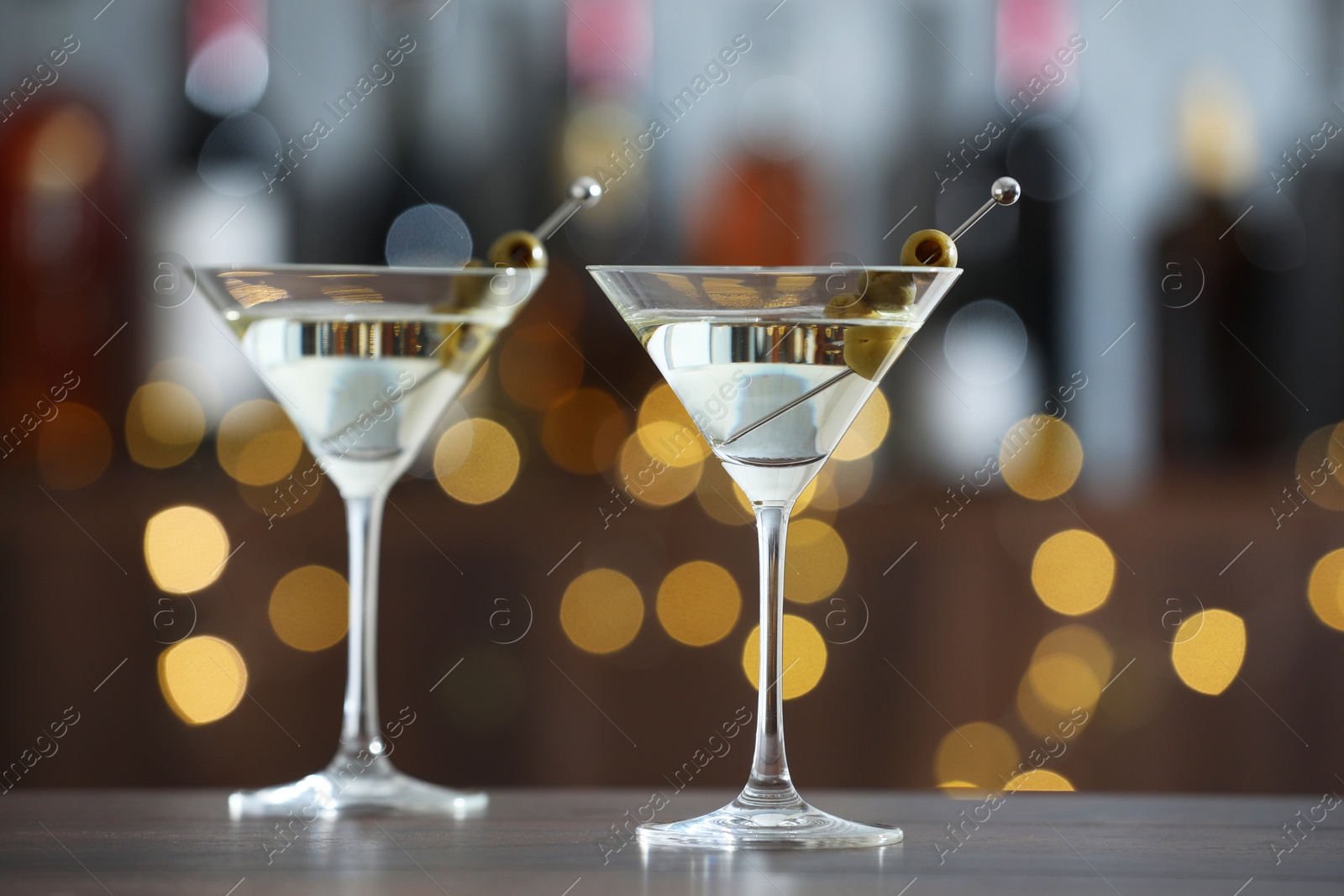 Photo of Martini cocktail with olives in glasses on wooden table against blurred background. Bokeh effect