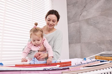 Smiling housewife with her daughter hanging clothes on drying rack at home