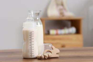 Photo of Milk in feeding bottle, jug and toy on wooden table indoors, space for text