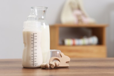 Photo of Milk in feeding bottle, jug and toy on wooden table indoors, space for text