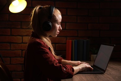 Woman in headphones working with laptop at table indoors