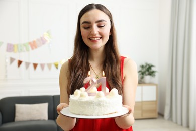 Coming of age party - 21st birthday. Happy young woman holding tasty cake with number shaped candles at home