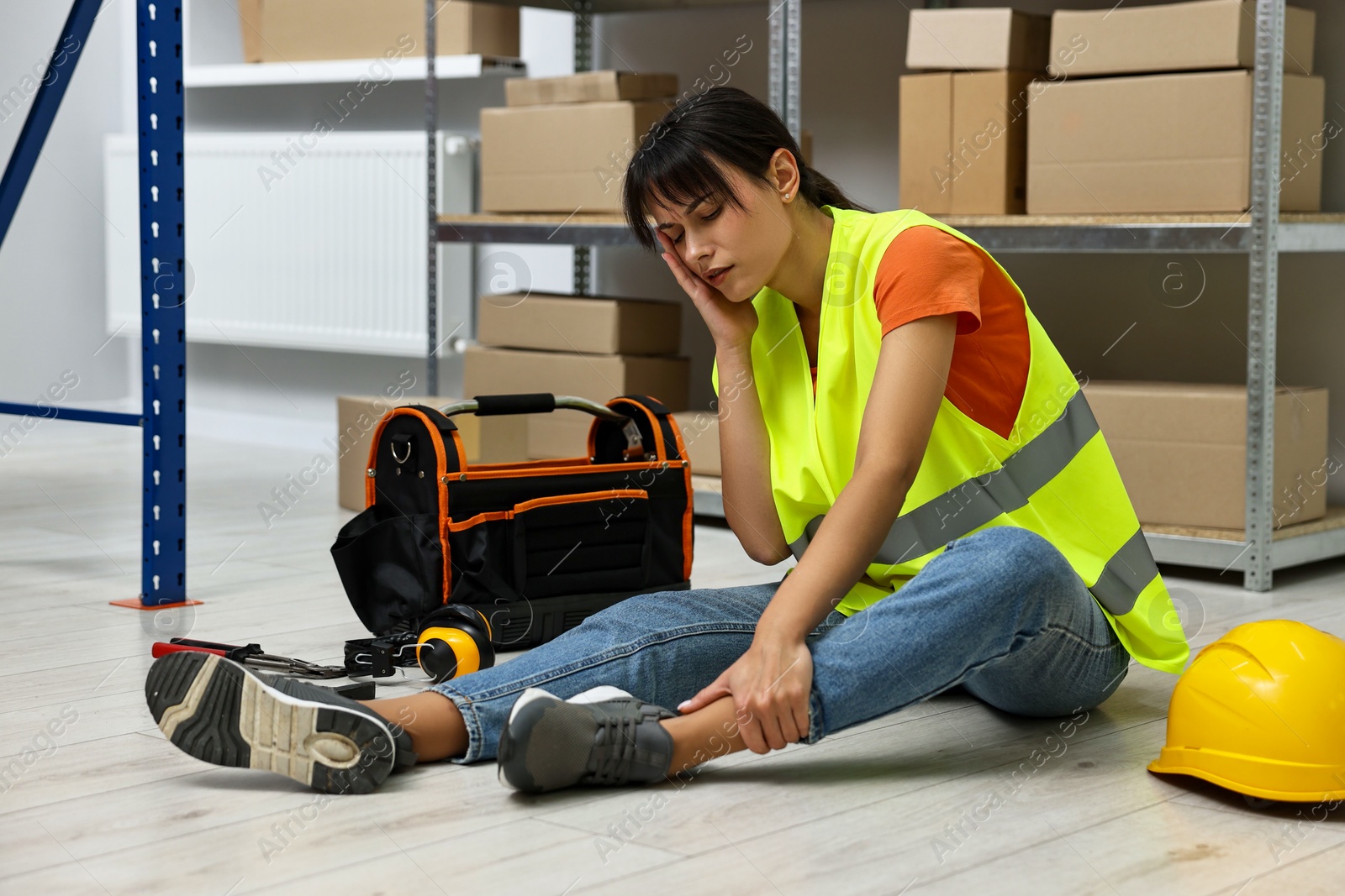 Photo of Accident at work. Injured woman with toolkit on floor in warehouse