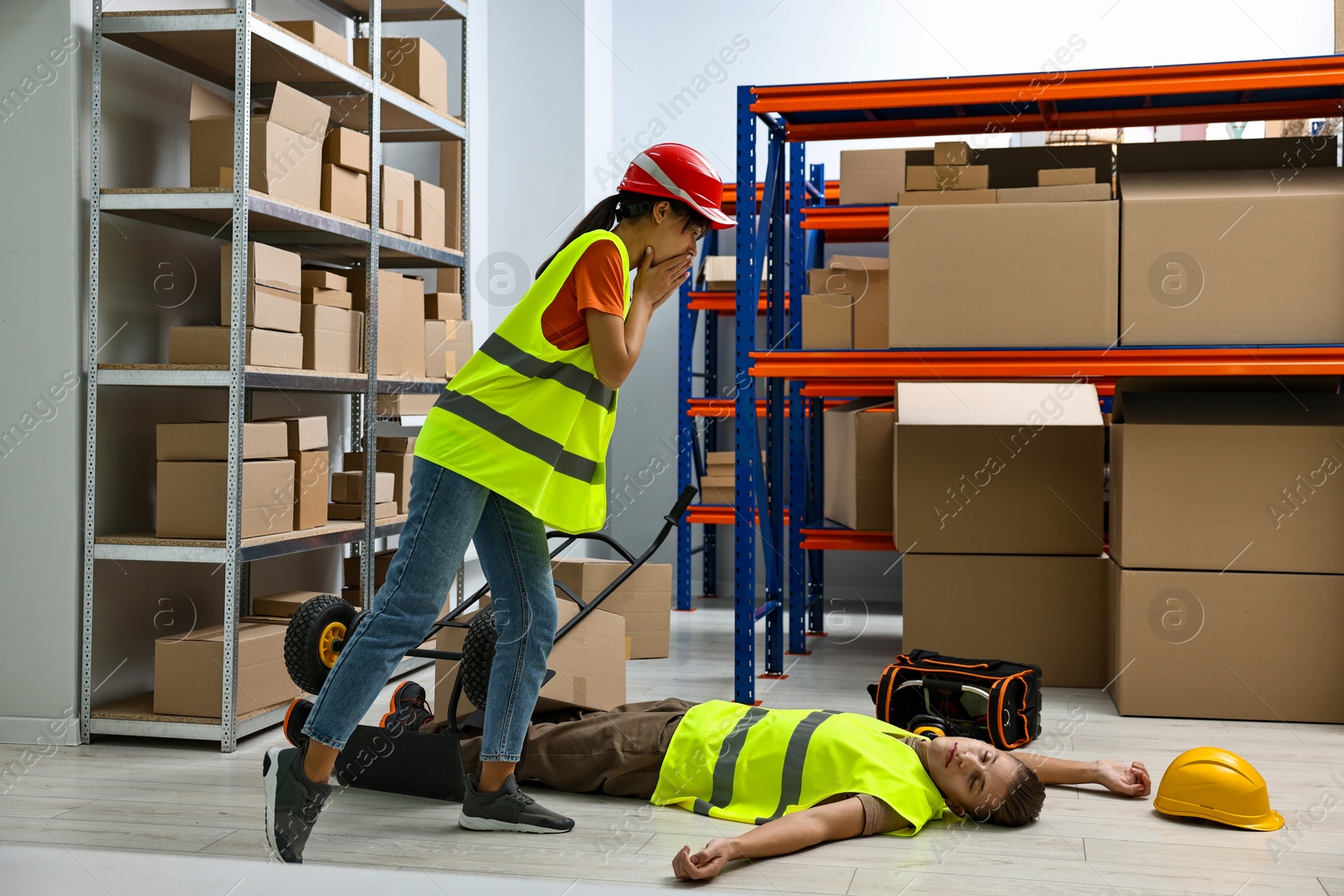 Photo of Accident at work. Worried woman and her unconscious colleague in warehouse