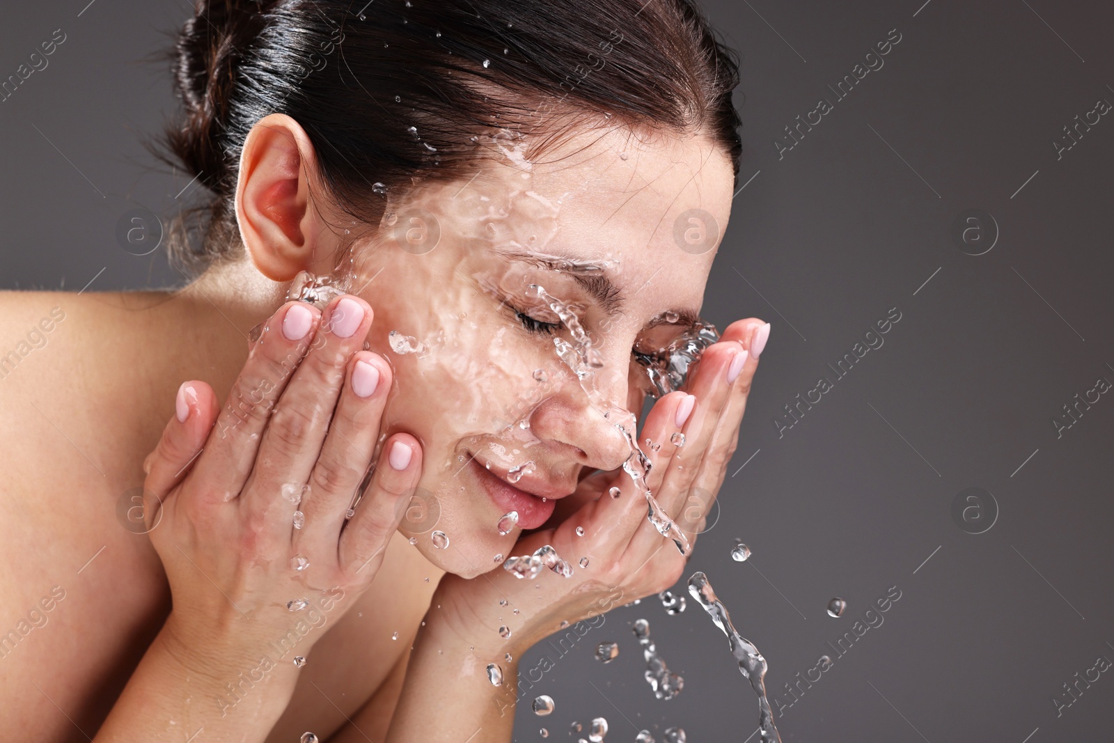 Photo of Attractive woman washing her face on grey background, space for text